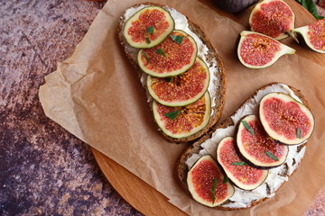 Fototapeta na wymiar Figs. Sandwiches with figs, cheese, arugula, honey and nuts on wooden board over textured purple backdrop. Homemade. Everyday autumn kitchen.