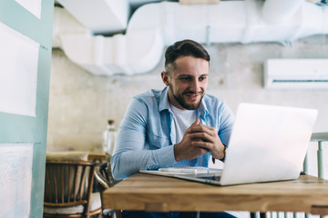Fototapeta premium Young man looking with pleasure at laptop in cafe