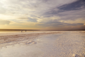 Unique landscape of a salt lake. Salt crystals on the shore and people walking in the water in the distance. Kuyalnik. Ukraine.
