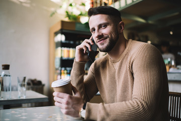Young charismatic man talking on mobile phone in cozy place