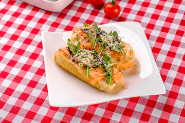 Italian Appetizer Bruschetta with Salmon, parmesan, balsamic vinegar and fresh arugula on white plate in italian restaurant background, top view. Italy food. Close up.