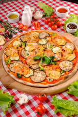 Vegetarian tasty pizza with vegetables, zucchini, eggplant, mushrooms, slices of tomato, fresh basil and tomatoes sauce on a wooden board, rustic village background, top view.