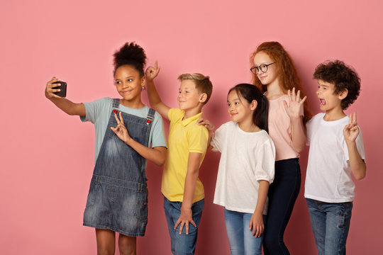 Multinational schoolkids taking selfie together over pink background