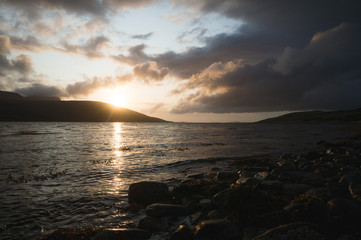 Sunset behind the mountains in font of a bay. Sun setting at the Scottish coast.