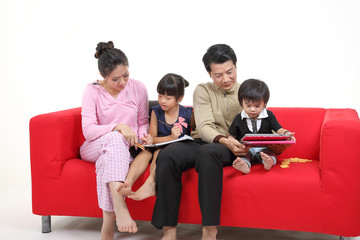 South East Asian young couple father mother son daughter parent girl boy child on red sofa read write study book use computer talk phone play tab on white background