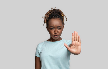 Angry african girl showing stop gesture over grey background