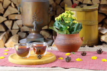 A couple glass mugs of black tea on the background of samovar, yellow tub and stack of firewood.
