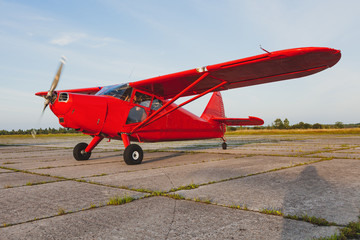 A vintage red small plane Stinson is preparing to take off on a private concrete runway.