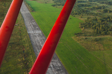 A vintage red small plane flies over a private concrete runway.