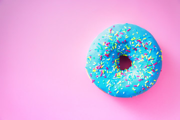 Overhead view of blue chocolate donut with sprinkles, isolated against colorful pink background,...