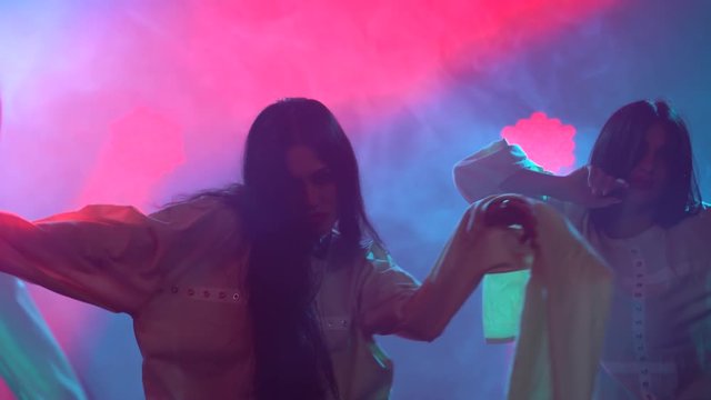 Silhouettes of a three charming womans in white shirt are dancing on the stage. Shot in a dark studio with smoke and neon lighting. Red neon light effects. Dance show.