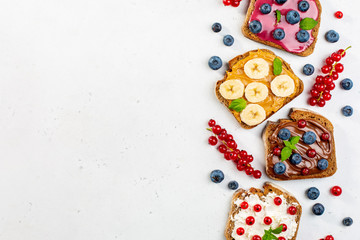 Variety of sweet sandwiches with peanut butter, chocolate butter, berry could, cream cheese, decorated with bananas, berries, mint.  Copy space.