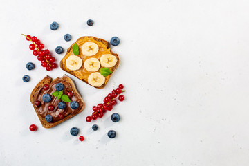 Sweet sandwiches with peanut butter and chocolate butter decorated with bananas, berries, mint. Copy space.
