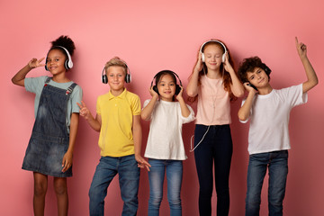 Multinational pupils in headsets enjoying music or listening to audio books over pink background