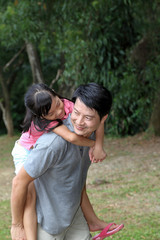 South East Asian young Chinese father daughter parent child playing activity outdoor park riding on fathers back piggyback ride love