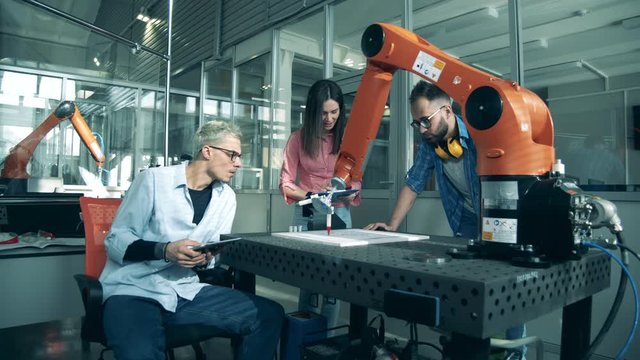 Innovation, hi-tech education, science studying concept. Robotic arm works at factory while people watch it.