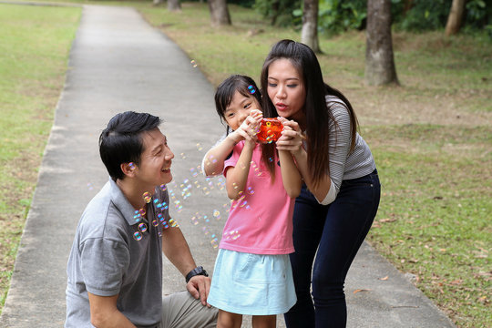 South East Asian Young Chinese Father Mother Daughter Parent Child Playing With Soap Bubbles Relax Activity Outdoor Park