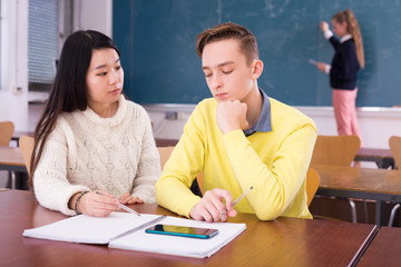 Fototapeta premium Intelligent asian teen girl explaining study material to her classmate in schoolroom