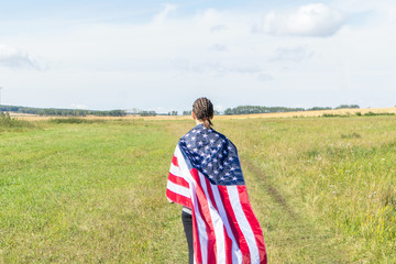 American young woman with afro-braids in a field of wheat wrapped in USA flag