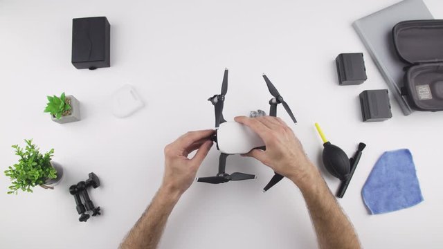 Top view, caucasian man install ND neutral density filter on drone DJI MAVIC AIR with his hand on white desk.