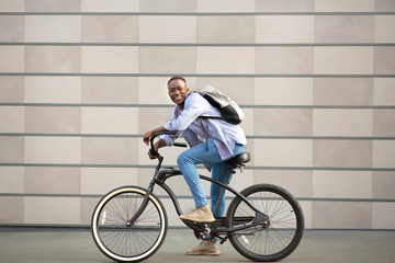 Portrait of joyful black guy with bicycle near brick wall outside