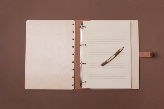 Opened big wooden notebook with pen ready to write on brown colored paper background. Top view