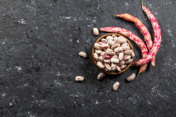 Harvested uncooked dried roman beans with raw pod plant on rustic background, heap of legume kidney...