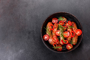 Grilled sausages with vegetables and spices on black background