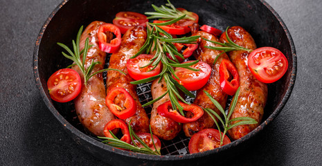 Grilled sausages with vegetables and spices on black background