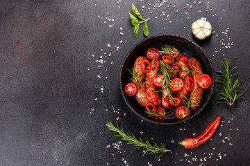 Grilled sausages with vegetables and spices on black background