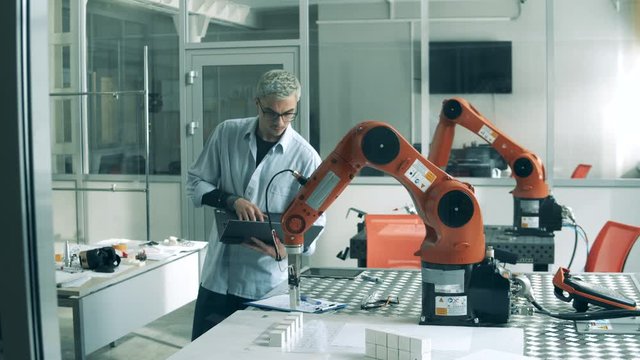 One person controls automated arm, using laptop in laboratory.