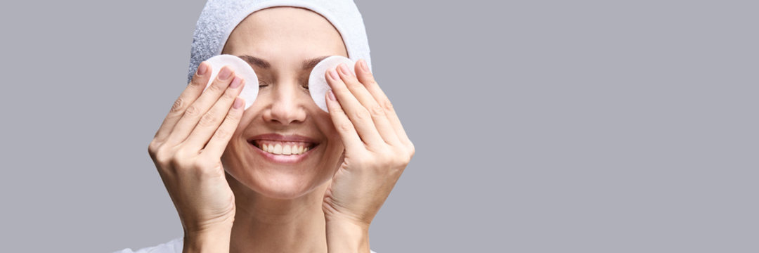 Cosmetology face cleaning. Female beautiful portrait. White cotton pad. Home facial routine. Remove make up. Demakeup toner. Foundation sponge. Cosmetics product. Grey. Horizontal banner. Copyspace