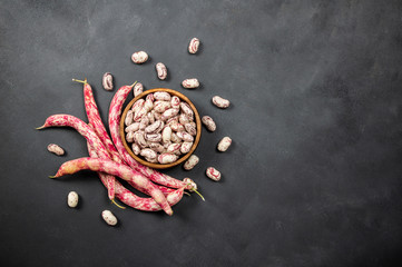 Harvested uncooked dried roman beans with raw pod plant on rustic background, heap of legume kidney...