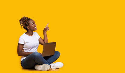 Young african woman with laptop pointing at empty space