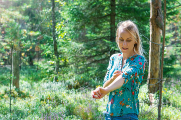 Portrait of blonde woman with colorful blouse in dense green forest and illuminated by summer sun beams