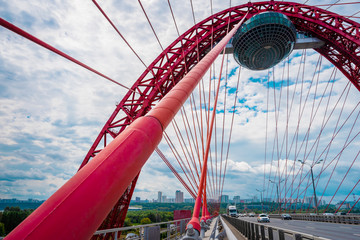 Moscow / Russia - 16 Aug 2020:  A picturesque bridge on a blue sky. Arched cable-stayed bridge of red color, on which the traffic flows