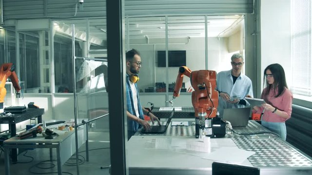 Men and a woman check robotic device working. Innovation, hi-tech education, science studying concept.