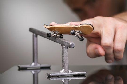 Man rolls a fingerboard on a gray metal railing
