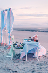 Vintage maritime wedding decoration on the northsea beach, boho white chair with pastell green covers, beautiful big bride bouquet, pink, blue, yellow roses and greenery in sand background. 