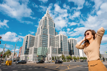 Fototapeta na wymiar Moscow / Russia - 16 Aug 2020: A young woman stands at a busy automobile intersection with a view of the glass business center building of multifunctional complex 
