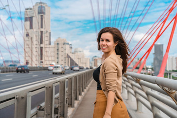 A young woman with long hair walks on a car bridge, metal red beams holding the structure