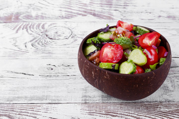 Salad with cucumbers, tomatoes, basil, red onion and olive oil in a wooden bowl on the white table