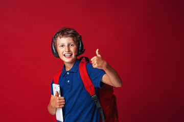 happy schoolboy in headphones with a microphone on a red background