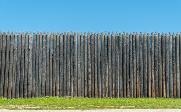 The fence is made of uncouth logs. palisade are rough and pointed to the top