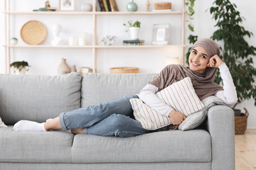 Relaxed arabic woman lying on couch at home, cuddling pillow, enjoying weekend