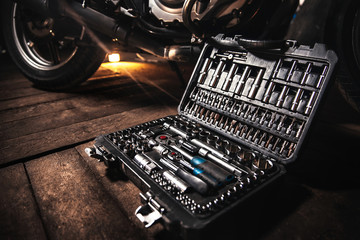 Close-up of a box with tools lies on the wooden floor against the backdrop of a motorcycle