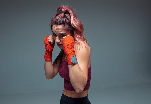 Portrait of female fighter in boxing bandages standing in studio isolated on gray background