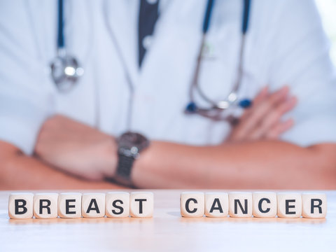Closeup wooden block written BREAST CANCER on table against professional male doctor with stethoscope. Physician ready to examine patient. Medical and patient care concept.