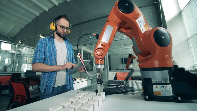 Male engineer controls robotic arm that moves cubes.