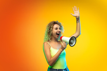 Shouting. Caucasian young woman's portrait isolated on gradient studio background in neon. Beautiful female curly model in casual style. Concept of human emotions, facial expression, youth, sales, ad.